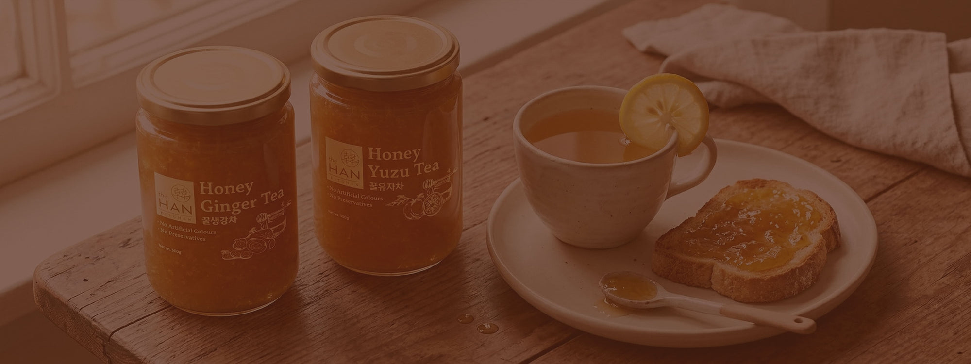 Two jars of honey, a cup of tea with lemon, and toast on a wooden table.