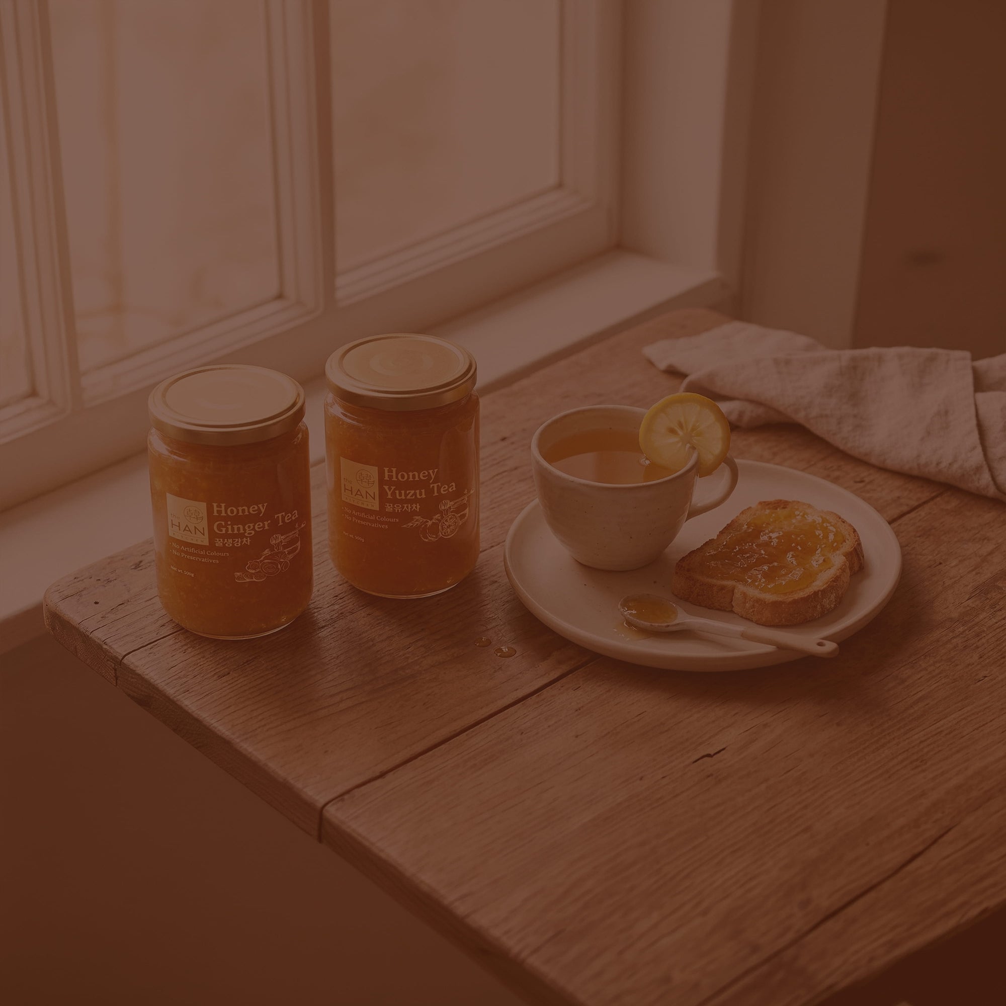 Two jars of honey and a cup with toast on a wooden surface.