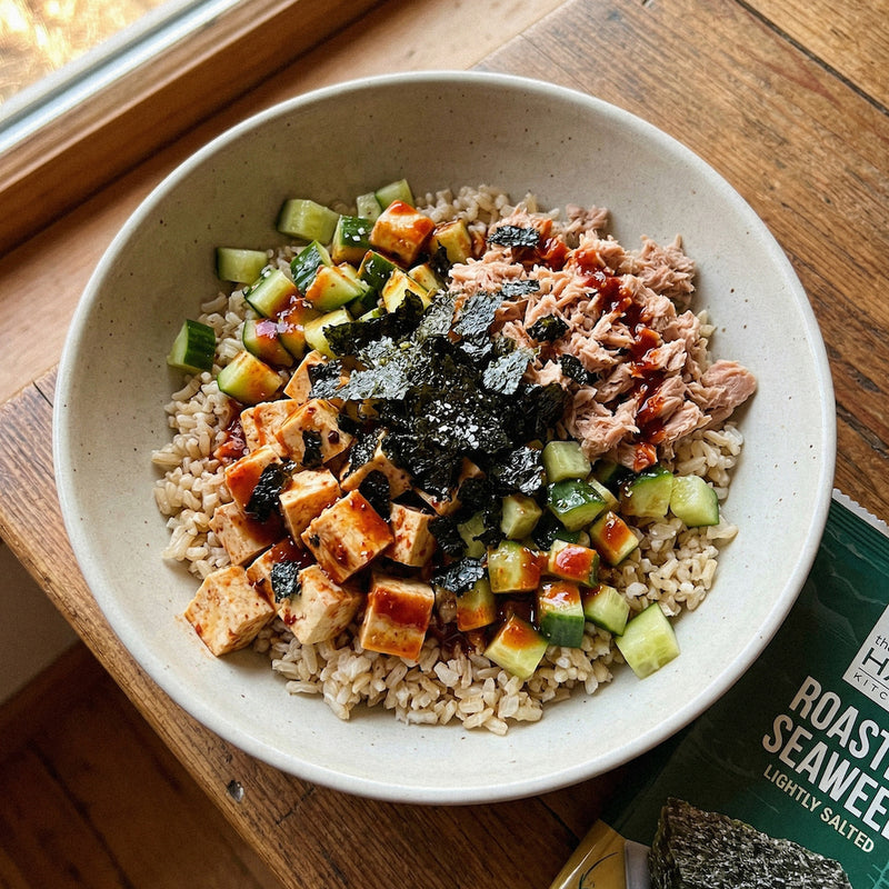 Bowl of food with rice, vegetables, and tofu on a wooden surface